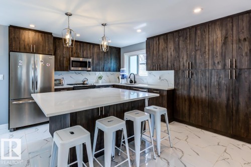 The kitchen features extensive dark wood cabinetry, a large kitchen island with a light-colored countertop, and stainless steel appliances - 9526 109A Avenue, Edmonton, AB - Indoor Photo Showing Kitchen