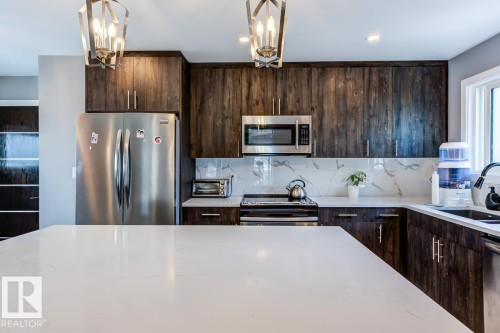 Kitchen featuring dark wood cabinetry, a white quartz countertop, stainless steel appliances, and a marble-patterned backsplash - 9526 109A Avenue, Edmonton, AB - Indoor Photo Showing Kitchen With Upgraded Kitchen