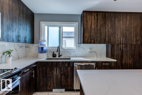 The kitchen features dark wood cabinetry, white countertops with marble-look veining, and a stainless steel dishwasher - 9526 109A Avenue, Edmonton, AB - Indoor Photo Showing Kitchen