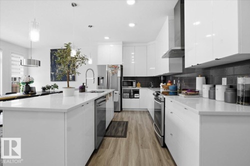 The kitchen features white cabinetry, stainless steel appliances, light-colored countertops, and wood-look flooring - 16624 32 Avenue, Edmonton, AB - Indoor Photo Showing Kitchen With Stainless Steel Kitchen With Upgraded Kitchen