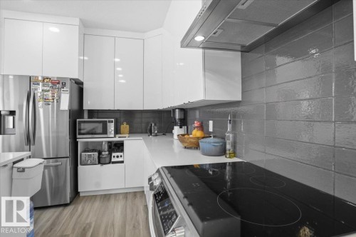 The kitchen features white cabinetry, a stainless steel refrigerator, and a gray tiled backsplash - 16624 32 Avenue, Edmonton, AB - Indoor Photo Showing Kitchen With Stainless Steel Kitchen With Upgraded Kitchen