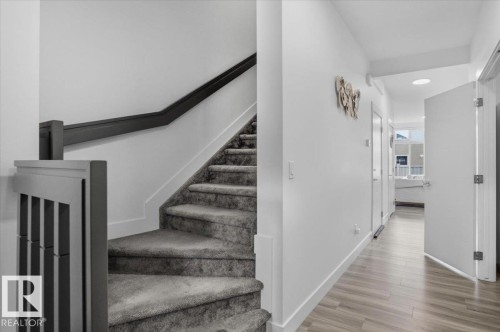 The property features a staircase with carpeted steps and a dark-colored handrail, leading to a hallway with light wood-look flooring and white walls - 16624 32 Avenue, Edmonton, AB - Indoor Photo Showing Other Room