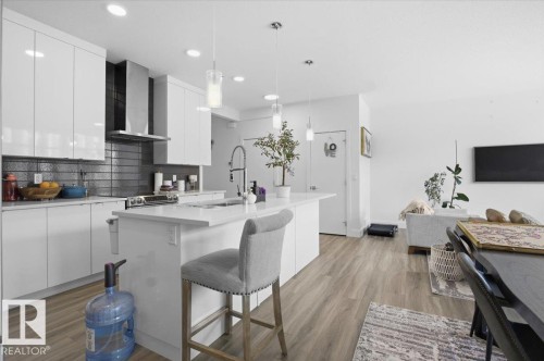 This kitchen features sleek white cabinetry, a dark tiled backsplash, and stainless steel appliances - 16624 32 Avenue, Edmonton, AB - Indoor Photo Showing Kitchen With Upgraded Kitchen