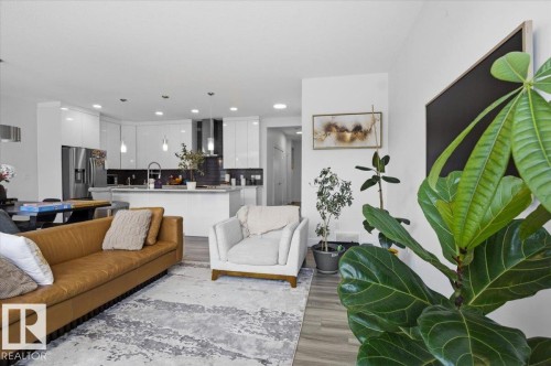 Open concept living area with light-toned flooring, featuring a modern kitchen with a central island, stainless steel appliances, and sleek white cabinetry - 16624 32 Avenue, Edmonton, AB - Indoor Photo Showing Living Room