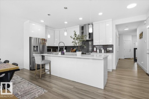 Modern kitchen featuring white cabinetry, a large kitchen island with a sink, stainless steel appliances, and sleek pendant lighting - 16624 32 Avenue, Edmonton, AB - Indoor Photo Showing Kitchen With Upgraded Kitchen