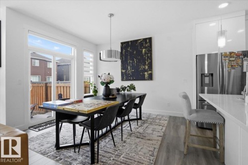Open concept dining area featuring a modern black dining table with seating, a large sliding glass door with a view of the fenced yard, and light-toned flooring - 16624 32 Avenue, Edmonton, AB - Indoor Photo Showing Dining Room