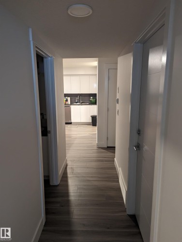 Hallway featuring dark wood flooring and white walls, leading towards a view of the kitchen with white cabinetry and stainless steel appliances - 16624 32 Avenue, Edmonton, AB - Indoor Photo Showing Other Room