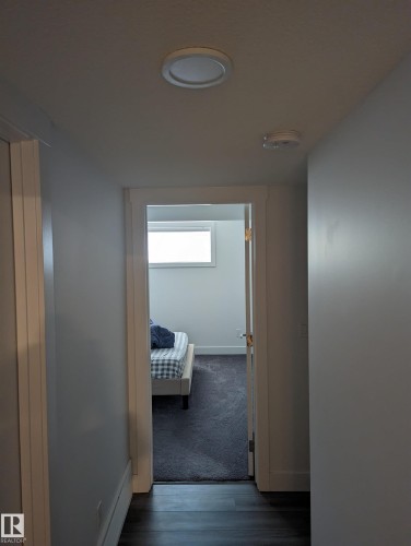 A hallway with dark wood flooring leads to a room featuring dark carpeting and a window - 16624 32 Avenue, Edmonton, AB - Indoor