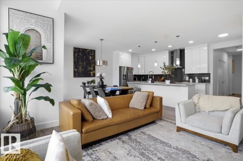 Open concept living area with light-colored flooring, leading to a modern kitchen with white cabinetry and an island - 16624 32 Avenue, Edmonton, AB - Indoor Photo Showing Living Room