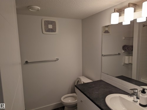 Bathroom featuring a vanity with a dark countertop, a white sink with a chrome faucet, and a large mirror with contemporary light fixtures - 16624 32 Avenue, Edmonton, AB - Indoor Photo Showing Bathroom