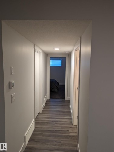 This hallway features resilient flooring and light-toned walls, leading towards a room with a window providing natural light - 16624 32 Avenue, Edmonton, AB - Indoor Photo Showing Other Room