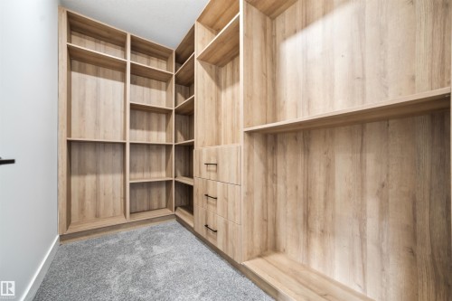 Well-appointed closet featuring extensive light wood-toned shelving, built-in drawers with dark hardware, and soft gray carpeting - 423 Robinson Boulevard, Leduc, AB - Indoor