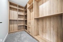 Well-appointed closet featuring extensive light wood-toned shelving, built-in drawers with dark hardware, and soft gray carpeting - 