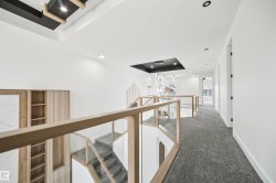 Upper level landing featuring a modern glass and wood railing, recessed lighting, and a view of the stairwell - 