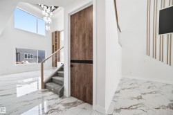 Entrance featuring white marble-style flooring, a carpeted staircase with a clear panel and wooden handrail, and a tall wooden door with a dark accent strip - 