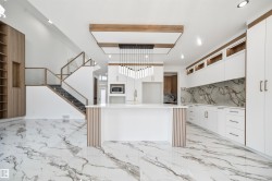 A spacious open-concept living area featuring marble-style flooring, a contemporary kitchen with white cabinetry and a central island, and a modern staircase with glass railings - 