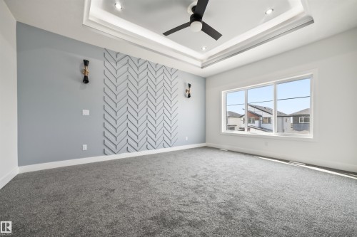 This room features a decorative accent wall with a chevron pattern, a tray ceiling with recessed lighting, and a modern ceiling fan - 423 Robinson Boulevard, Leduc, AB - Indoor Photo Showing Other Room