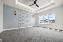 This room features a decorative accent wall with a chevron pattern, a tray ceiling with recessed lighting, and a modern ceiling fan - 