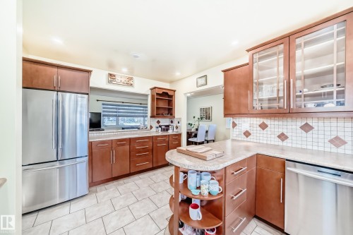 The kitchen features tile flooring, wood cabinetry with some glass-fronted upper cabinets, a tiled backsplash, and stainless steel appliances - 4446 116 Avenue, Edmonton, AB 