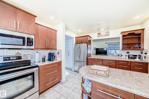 The kitchen features wood cabinetry, stainless steel appliances, and a tiled backsplash - 4446 116 Avenue, Edmonton, AB 