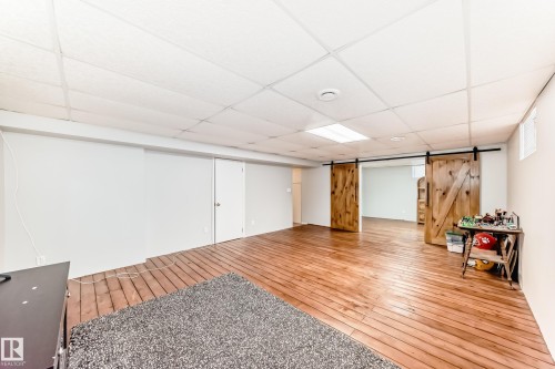 This expansive room features wide plank wood flooring and modern barn-style sliding doors, enhancing its unique appeal - 4446 116 Avenue, Edmonton, AB 