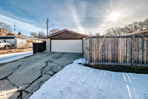 The property features a detached garage with a white garage door, a wooden privacy fence, and a paved driveway - 4446 116 Avenue, Edmonton, AB 