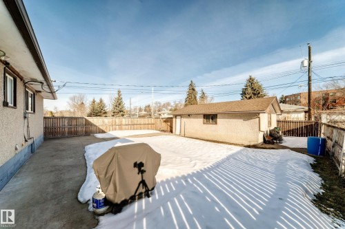 The property features an extensive backyard with a concrete patio, a wooden fence, and a detached garage with a brown roof - 4446 116 Avenue, Edmonton, AB 