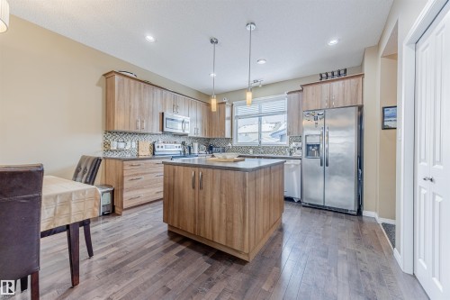 Kitchen featuring loads of modern cabinets, S/S appliances, a large center island with pendant lighting, tile backsplash, large pantry & hardwood flooring. - 1312 74 Street, Edmonton, AB - Indoor Photo Showing Kitchen