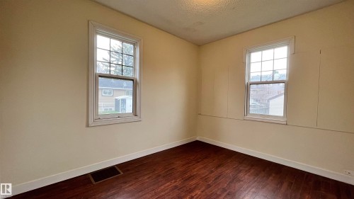 This room features two windows providing natural light, warm-toned walls, and dark wood-look flooring - 10839 109 Street, Edmonton, AB - Indoor Photo Showing Other Room