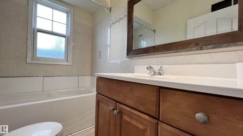 Bathroom with a window, white bathtub, and wood vanity with a white countertop and framed mirror - 10839 109 Street, Edmonton, AB - Indoor Photo Showing Bathroom