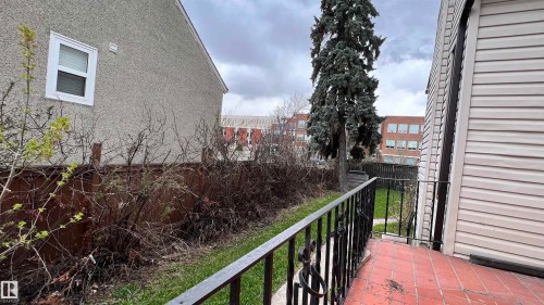 Exterior property view featuring a side yard with a lawn, a mature evergreen tree, and a tiled path leading to an entrance with an iron railing - 10839 109 Street, Edmonton, AB - Outdoor