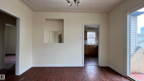 Bright room with dark hardwood flooring, featuring a wall niche with a mirror, a doorway leading to a kitchen with wooden cabinetry, and access to an outdoor area with views of surrounding buildings - 10839 109 Street, Edmonton, AB - Indoor Photo Showing Other Room