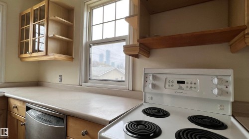 The kitchen features light-colored countertops, wood cabinetry, a window providing natural light, and a white electric range - 10839 109 Street, Edmonton, AB - Indoor Photo Showing Kitchen