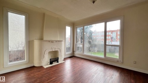Living room featuring rich hardwood flooring, a decorative fireplace, and large windows providing natural light - 10839 109 Street, Edmonton, AB - Indoor Photo Showing Other Room