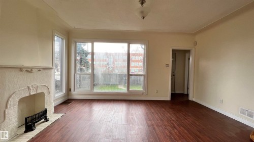 The living room features an ornate fireplace, dark wood flooring, and large windows that provide views of the outdoors - 10839 109 Street, Edmonton, AB - Indoor Photo Showing Other Room