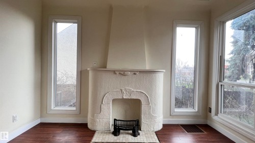 Living room featuring a decorative fireplace with a mantel, dark wood flooring, and tall windows providing natural light - 10839 109 Street, Edmonton, AB - Indoor Photo Showing Other Room