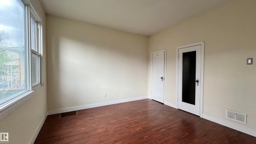 This room features rich wood flooring, neutral-toned walls, and a large window providing natural illumination - 10839 109 Street, Edmonton, AB - Indoor Photo Showing Other Room
