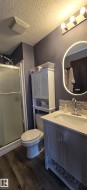 Bathroom featuring a vanity with a white countertop and a contemporary faucet, a shower with a clear and frosted glass door, and dark wood-look flooring - 