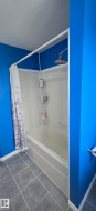 The bathroom features a shower-over-bath unit with a curved shower curtain rod, a mounted shower head, and tiled flooring - 