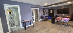 This versatile space features light-toned flooring, exposed wooden beams, and a wall-mounted television - 