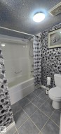 Bathroom featuring a bathtub with an integrated shower, tiled flooring, and a toilet - 