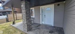 Covered front entry featuring a stone-clad pillar, stamped concrete patio, horizontal siding, and a white entry door with sidelite - 