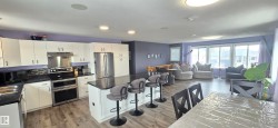 This open-concept living space features a kitchen with white cabinetry and stainless steel appliances, a kitchen island with seating, and wood-look flooring throughout - 