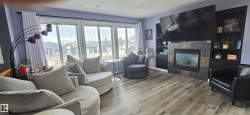 Living area featuring large windows, wood-look flooring, and a fireplace with tile surround - 