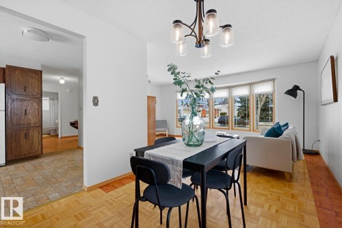 Bright dining area with parquet flooring, an overhead chandelier with clear glass shades, and a partial view of a living space featuring a bay window - 16108 100 Street, Edmonton, AB - Indoor Photo Showing Dining Room
