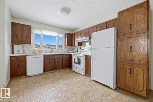 The kitchen features ample cabinetry, a window providing natural light, and white appliances including a refrigerator, stove, and dishwasher - 16108 100 Street, Edmonton, AB - Indoor Photo Showing Kitchen