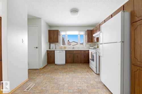 The kitchen features wood cabinetry, white appliances, and a window above the sink - 16108 100 Street, Edmonton, AB - Indoor Photo Showing Kitchen With Double Sink