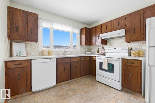 The kitchen features extensive wood cabinetry, a white dishwasher, and a white range with an overhead exhaust fan - 16108 100 Street, Edmonton, AB - Indoor Photo Showing Kitchen