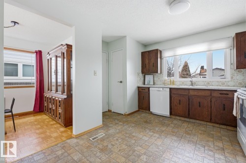 The kitchen features dark wood cabinetry, a white dishwasher, and a large window providing natural light - 16108 100 Street, Edmonton, AB - Indoor Photo Showing Kitchen