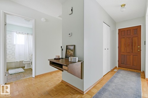 The property features warm hardwood flooring, a substantial paneled wooden entry door, and a bathroom with a window and a bathtub with a shower - 16108 100 Street, Edmonton, AB - Indoor Photo Showing Other Room